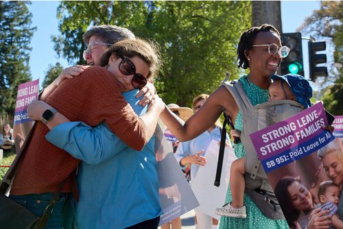 Advocate and legislative staffer embrace at a rally outside the California state capitol after learning that SB 951, raising California&#x27;s paid leave wage replacement rates, has become law.